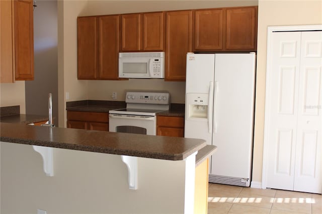 kitchen featuring a kitchen bar, white appliances, kitchen peninsula, and light tile patterned floors