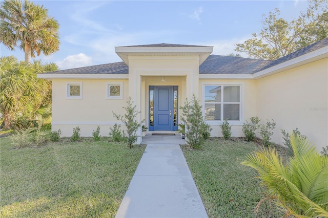 doorway to property featuring a shingled roof, a yard, and stucco siding