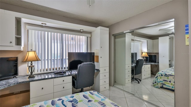 bedroom featuring a textured ceiling, built in desk, a closet, and light tile patterned flooring