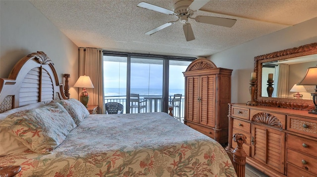 bedroom with ceiling fan, expansive windows, a textured ceiling, access to outside, and a water view