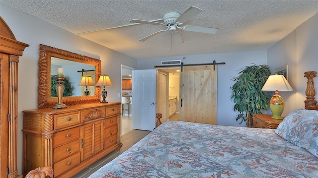 bedroom featuring ceiling fan, a barn door, a textured ceiling, and light hardwood / wood-style flooring