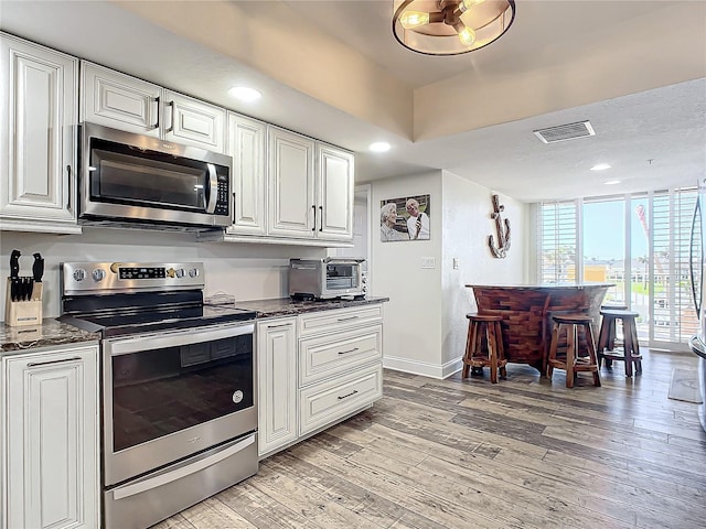 kitchen featuring appliances with stainless steel finishes, light wood-type flooring, white cabinetry, and dark stone counters