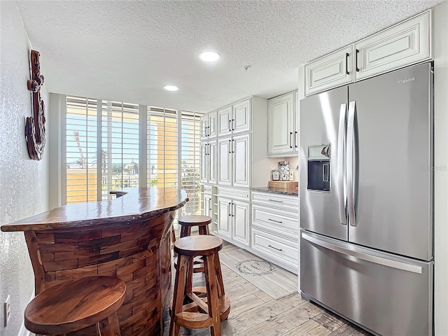 kitchen with a textured ceiling, white cabinets, stainless steel refrigerator with ice dispenser, and light hardwood / wood-style flooring