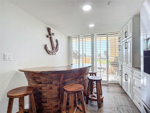 bar featuring light hardwood / wood-style floors, white cabinetry, and a textured ceiling