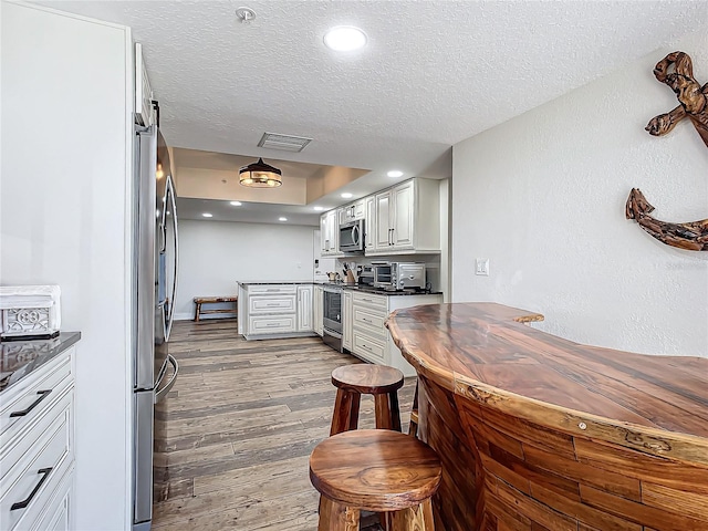 kitchen with white cabinetry, stainless steel appliances, a textured ceiling, and light wood-type flooring