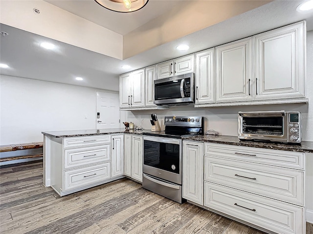 kitchen with kitchen peninsula, white cabinetry, stainless steel appliances, and light hardwood / wood-style flooring