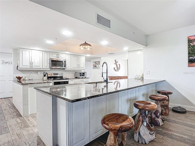 kitchen with kitchen peninsula, appliances with stainless steel finishes, light wood-type flooring, sink, and white cabinets