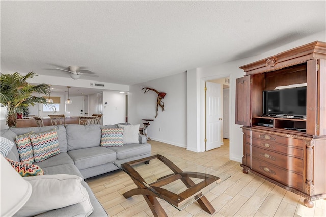 living room with ceiling fan, a textured ceiling, and light wood-type flooring