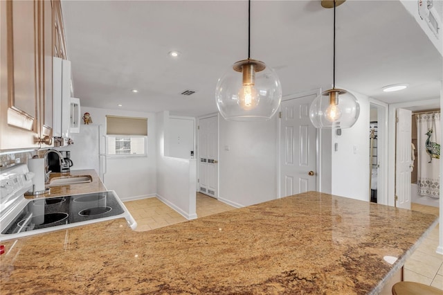 kitchen featuring light stone countertops, sink, kitchen peninsula, stove, and decorative light fixtures