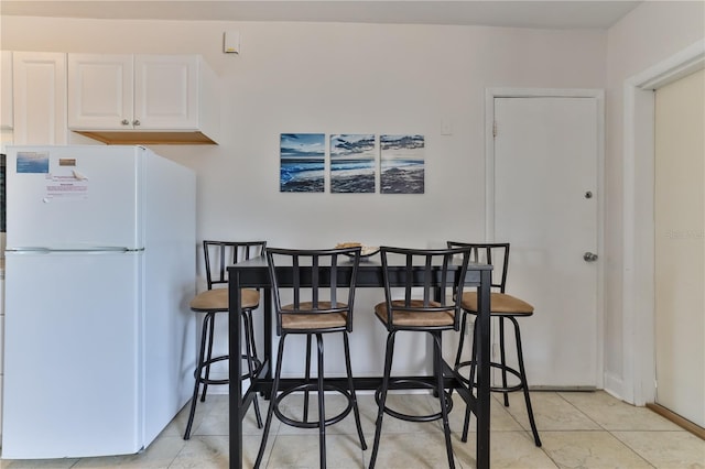 kitchen with a breakfast bar, white refrigerator, and white cabinetry