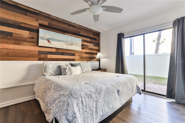 bedroom with access to outside, dark hardwood / wood-style floors, ceiling fan, and wood walls