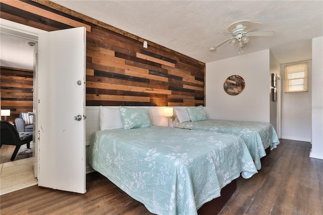 bedroom with ceiling fan, wood walls, and dark wood-type flooring