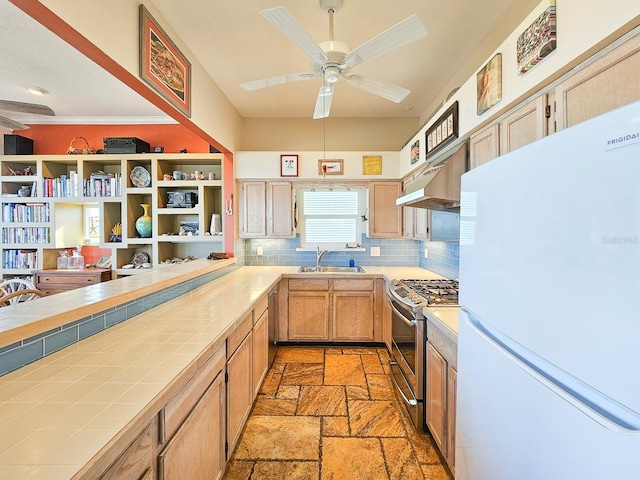 kitchen with ceiling fan, sink, stainless steel gas range oven, white refrigerator, and tile countertops