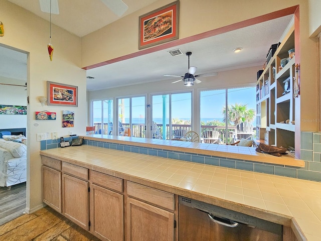 kitchen with tile countertops, stainless steel dishwasher, a fireplace, light hardwood / wood-style floors, and kitchen peninsula