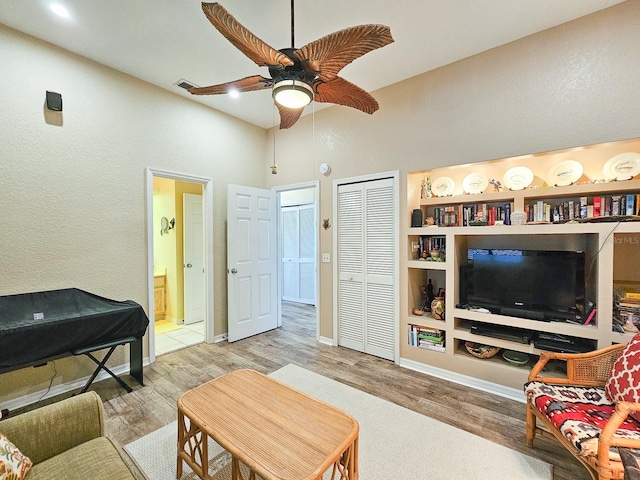 living room with ceiling fan, a towering ceiling, and light hardwood / wood-style flooring