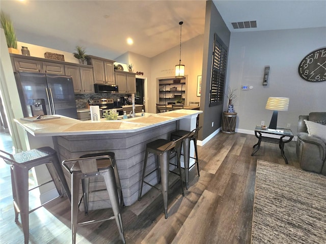 kitchen featuring appliances with stainless steel finishes, dark hardwood / wood-style floors, vaulted ceiling, and a breakfast bar area