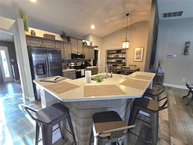 kitchen featuring appliances with stainless steel finishes, dark hardwood / wood-style floors, a large island with sink, and lofted ceiling