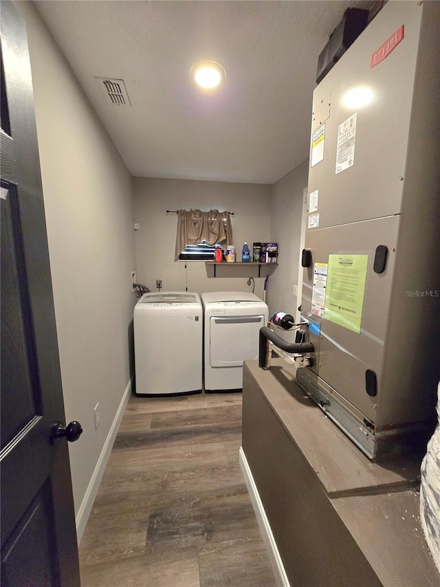 clothes washing area with hardwood / wood-style flooring, heating unit, and washing machine and clothes dryer