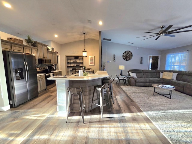 kitchen with an island with sink, vaulted ceiling, a breakfast bar area, appliances with stainless steel finishes, and hardwood / wood-style flooring