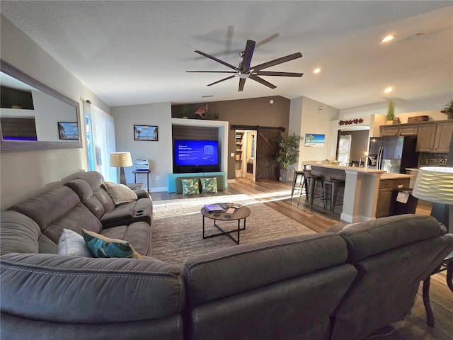 living room featuring ceiling fan, a barn door, lofted ceiling, and light hardwood / wood-style flooring