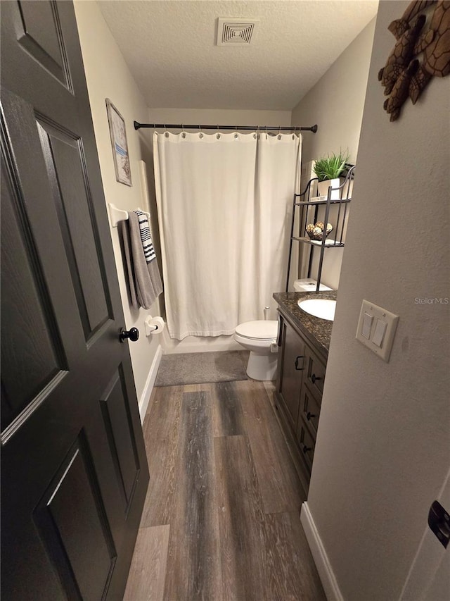 full bathroom with vanity, a textured ceiling, shower / bath combo with shower curtain, hardwood / wood-style floors, and toilet