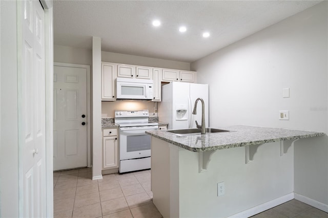 kitchen with a kitchen bar, a textured ceiling, white appliances, and white cabinets