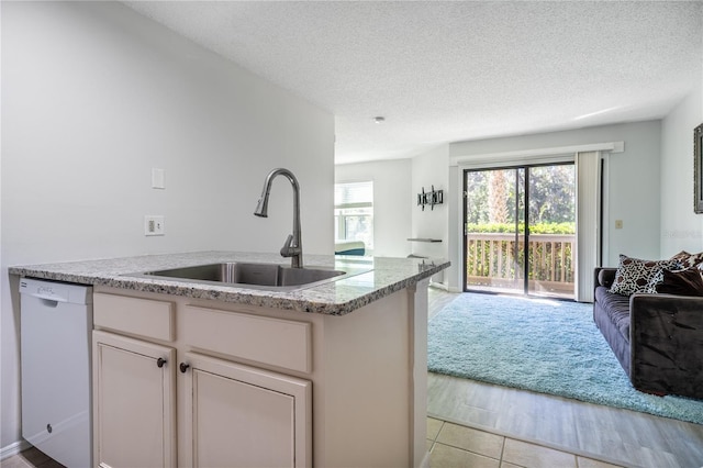 kitchen featuring dishwasher, sink, light stone counters, light hardwood / wood-style floors, and a textured ceiling