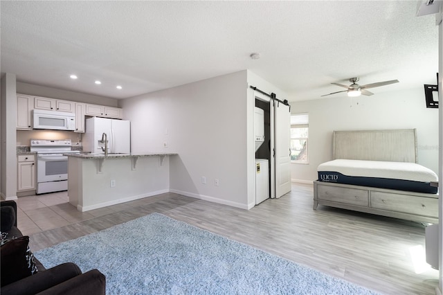 kitchen featuring white appliances, a barn door, light wood-type flooring, light stone counters, and a kitchen bar