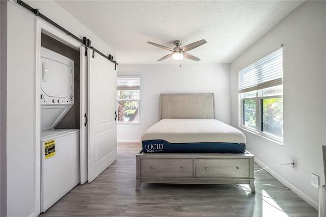 bedroom featuring dark hardwood / wood-style floors, a barn door, stacked washer and dryer, and multiple windows