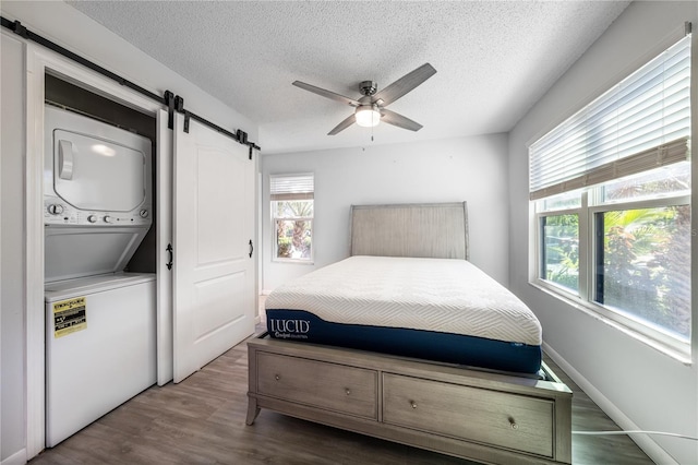 bedroom featuring stacked washer and clothes dryer, ceiling fan, a barn door, a textured ceiling, and wood-type flooring