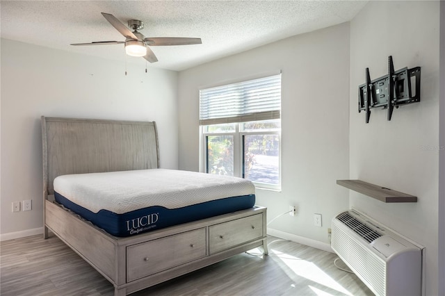 bedroom featuring ceiling fan, light hardwood / wood-style floors, a textured ceiling, and a wall mounted AC