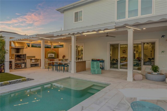 back house at dusk featuring a patio area, ceiling fan, a bar, and exterior kitchen