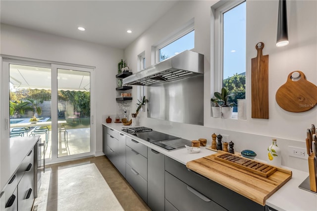 kitchen with pendant lighting, black stovetop, wall chimney exhaust hood, and gray cabinetry