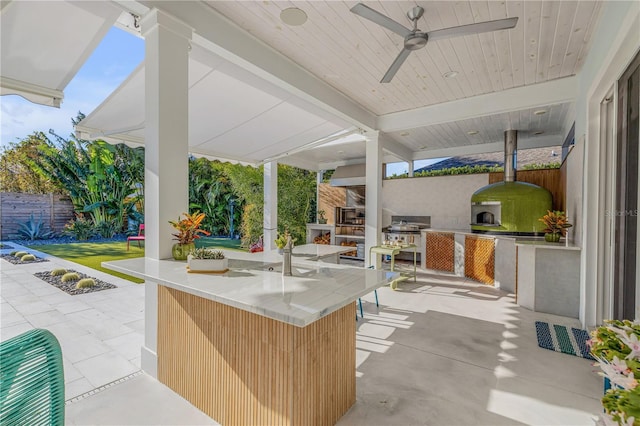 view of patio with a bar, an outdoor kitchen, and ceiling fan