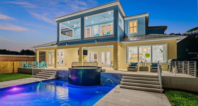 back house at dusk with pool water feature, a pool with hot tub, a patio, and french doors