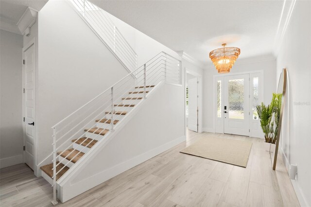 foyer with light hardwood / wood-style flooring, ornamental molding, and a notable chandelier