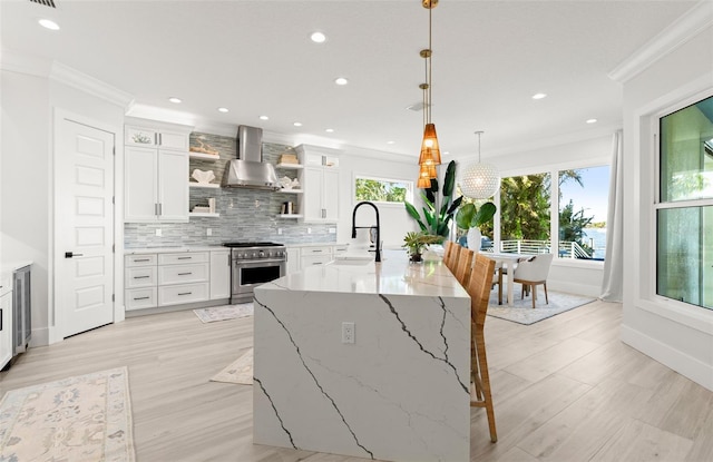 kitchen with white cabinets, high end stove, wall chimney exhaust hood, and sink