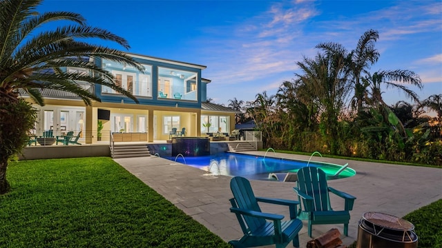 pool at dusk featuring french doors, pool water feature, a patio area, and a yard