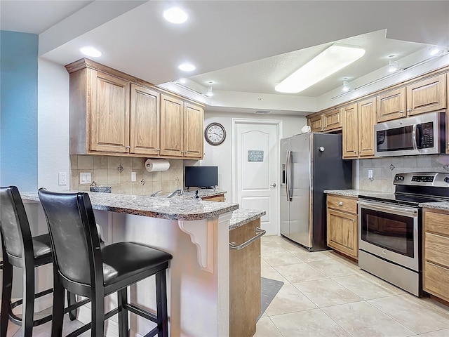 kitchen with stainless steel appliances, a kitchen breakfast bar, kitchen peninsula, decorative backsplash, and light tile patterned floors