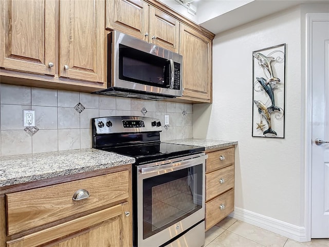 kitchen featuring light stone countertops, stainless steel appliances, tasteful backsplash, and light tile patterned flooring