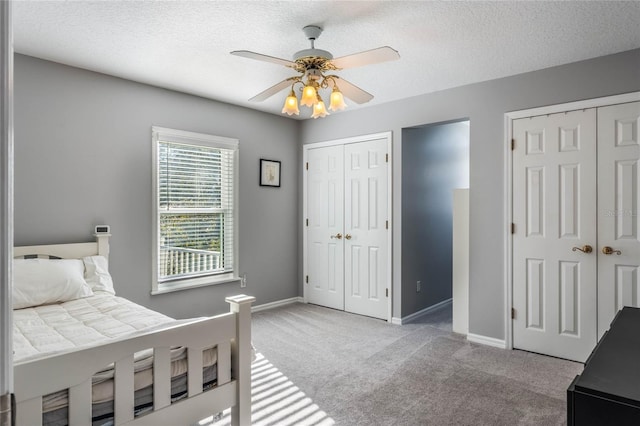 carpeted bedroom with a textured ceiling, two closets, and ceiling fan