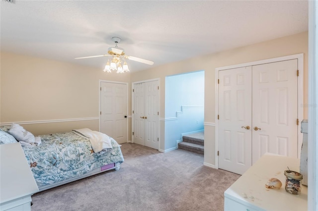 bedroom featuring light carpet, ceiling fan, and multiple closets