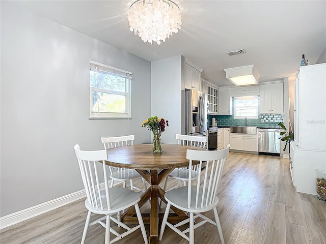 dining space featuring a healthy amount of sunlight, sink, a notable chandelier, and light wood-type flooring