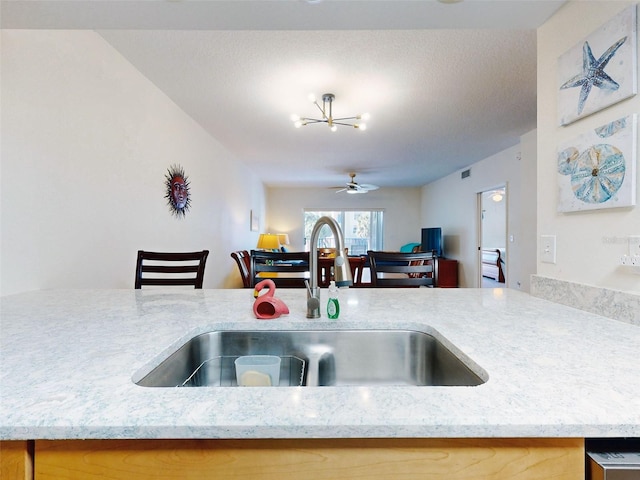 kitchen featuring a textured ceiling, light stone countertops, sink, and an inviting chandelier