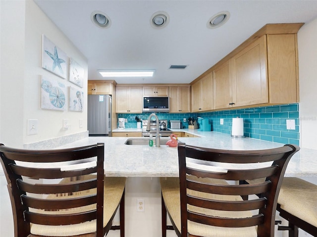 kitchen featuring light brown cabinets, sink, stainless steel appliances, a kitchen breakfast bar, and decorative backsplash