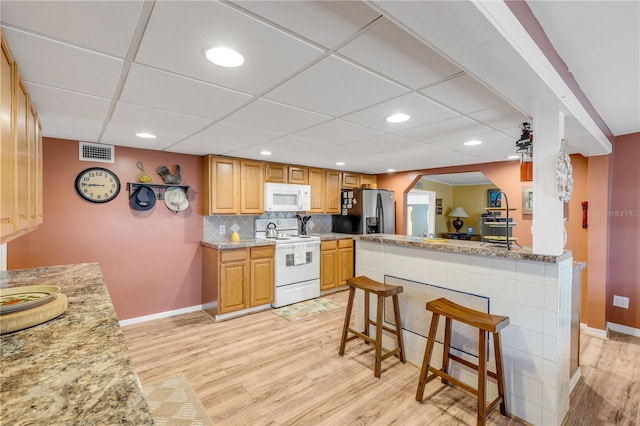 kitchen with kitchen peninsula, light stone countertops, a breakfast bar, white appliances, and light hardwood / wood-style flooring