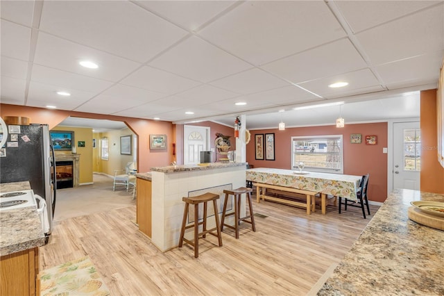 kitchen featuring decorative light fixtures, light stone counters, a breakfast bar area, and light hardwood / wood-style flooring