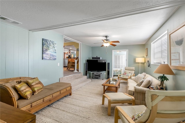 carpeted living room with ceiling fan, wood walls, and a textured ceiling