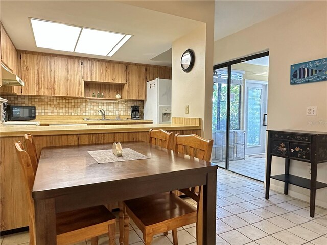 kitchen with kitchen peninsula, backsplash, sink, light tile patterned floors, and white fridge with ice dispenser