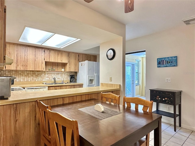 kitchen with decorative backsplash, kitchen peninsula, ceiling fan, white refrigerator with ice dispenser, and light tile patterned floors